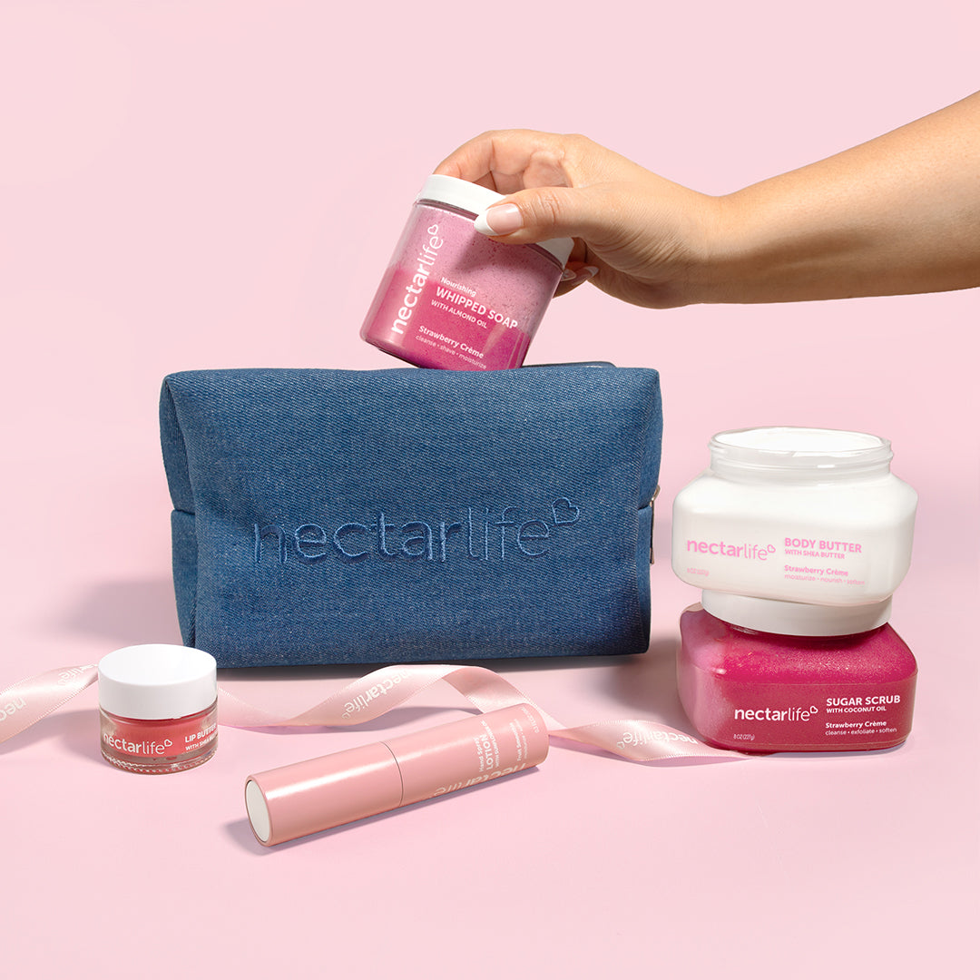 Hand placing Nectar Life Strawberry Crème products into a dark denim travel pouch, gift set with body butter and sugar scrub