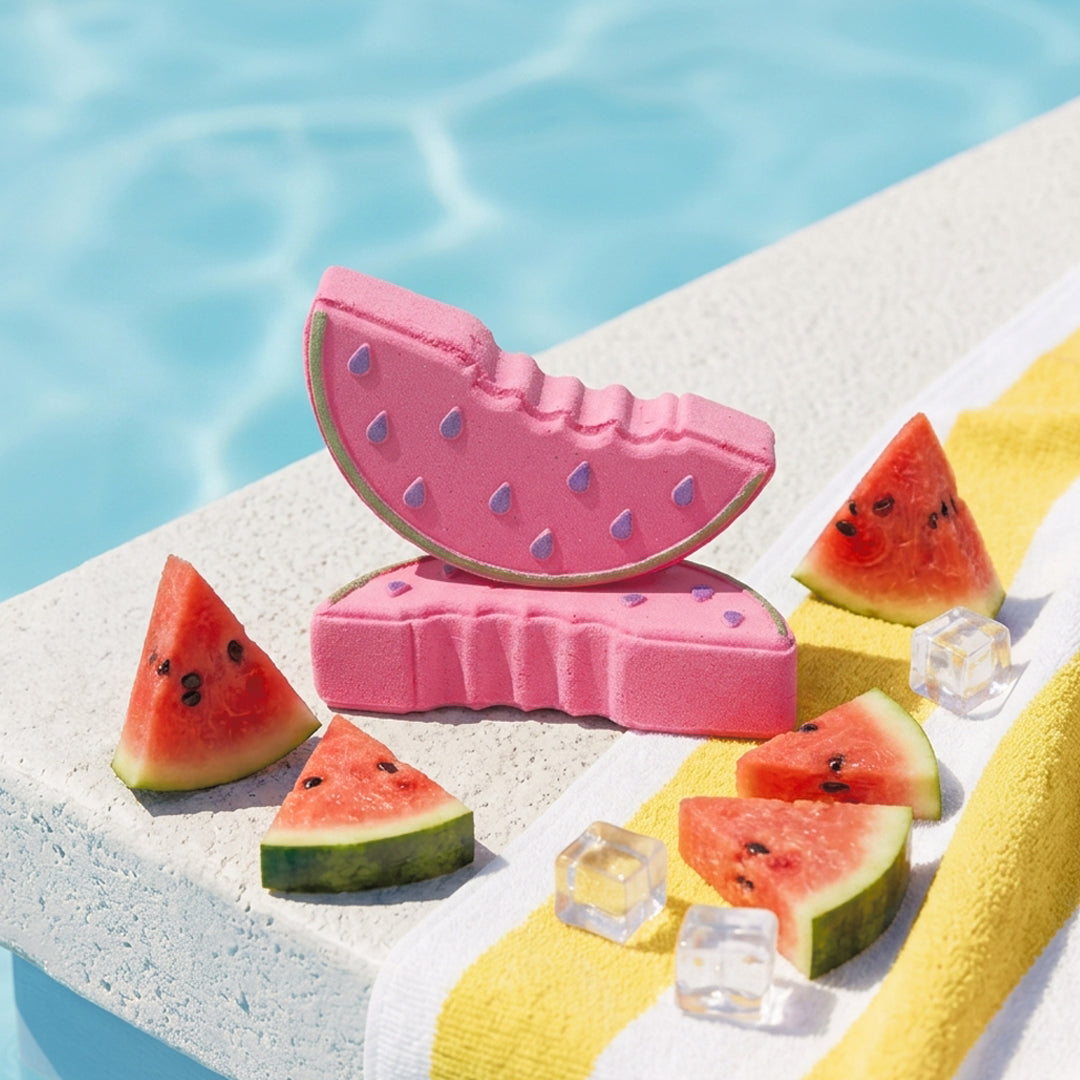 Nectar Life Fresh Watermelon Slice Bath Bombs on a sunny pool ledge surrounded by fresh watermelon slices and ice cubes, with a yellow striped towel and blue water in the background