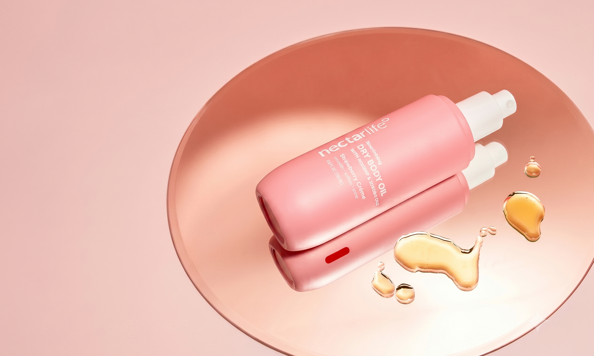 Pink bottle of Nectar Life dry body oil with rosehip and jojoba oils on a pink dish