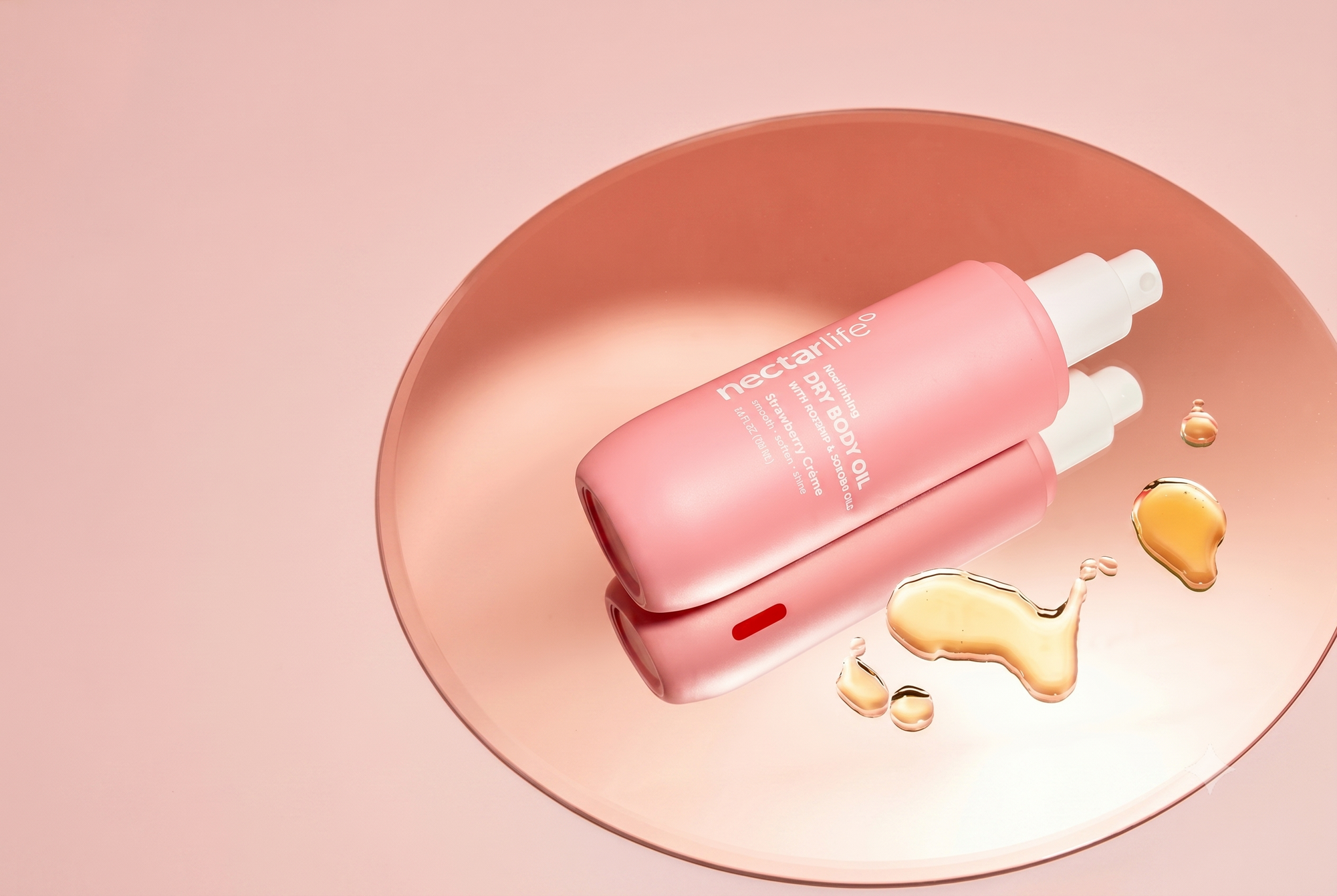 Pink bottle of Nectar Life dry body oil with rosehip and jojoba oils on a pink dish