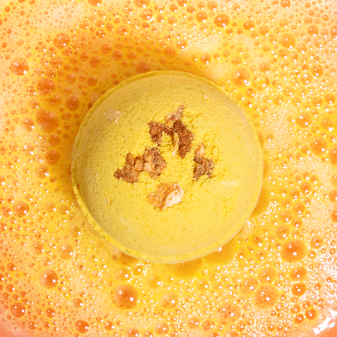 Nectar Life Citrus Sunrise Round Bath Bomb fizzing in warm water overhead view, releasing golden yellow color with grapefruit peel and Epsom salt, handmade in Las Vegas
