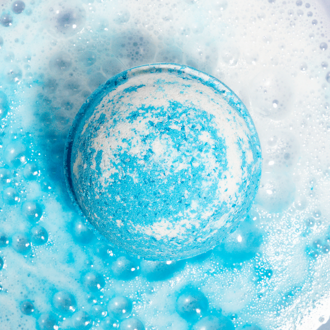 Nectar Life Ocean Breeze Round Bath Bomb fizzing in warm water overhead view, releasing bright blue color with Epsom salt and bentonite clay, handmade in Las Vegas