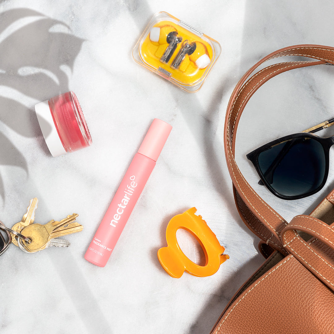 Nectar Life Custom Fragrance Mist in pink spray bottle alongside handbag and sunglasses, portable non-comedogenic body fragrance mist with safflower oil, handmade in USA