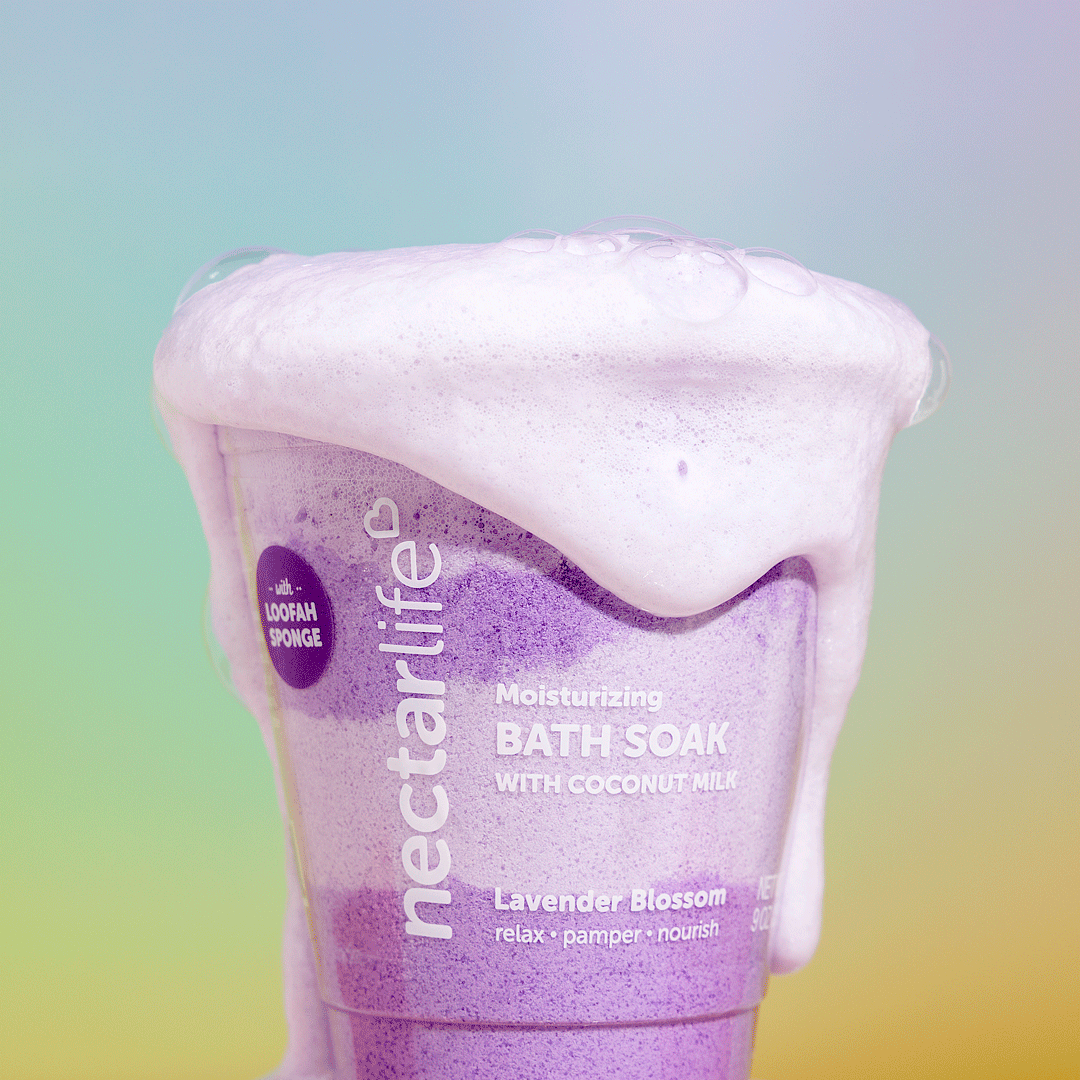 Nectar Life Moisturizing Milkshake Bath Soak in Lavender Blossom, foaming in warm bath water, purple swirling color
