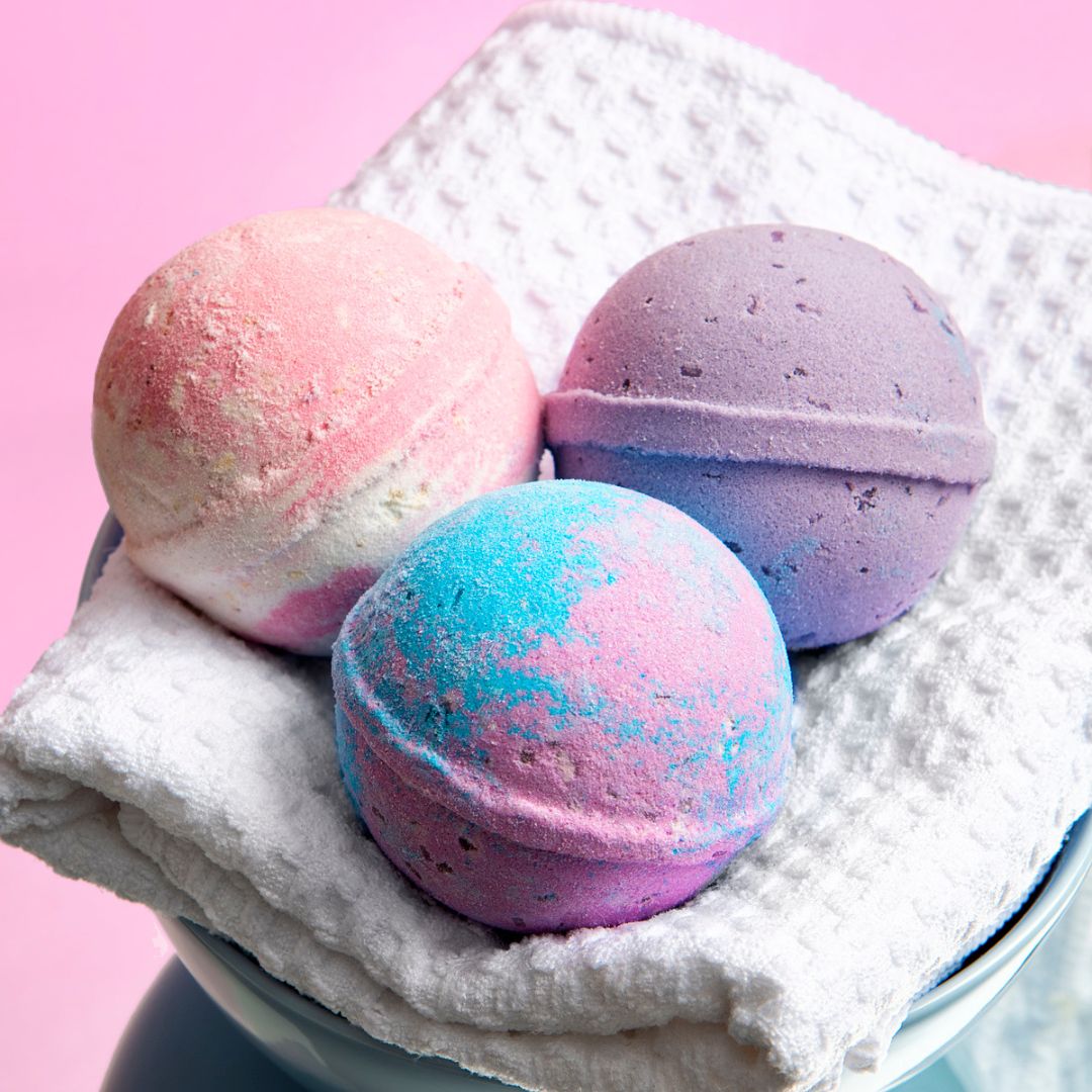 Three Nectar Life Round Bath Bombs in Exotic Acai, Lavender Blossom, and Coco Paradise scents displayed on a white waffle towel on a pink background, handmade in Las Vegas