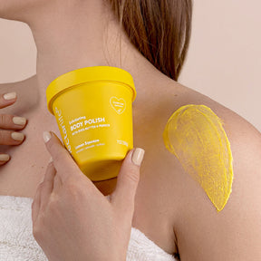 Nectar Life Body Polish being applied to shoulder in circular motions, Lemon Squeeze scent yellow tub, exfoliating ground pumice with shea butter and jojoba oil
