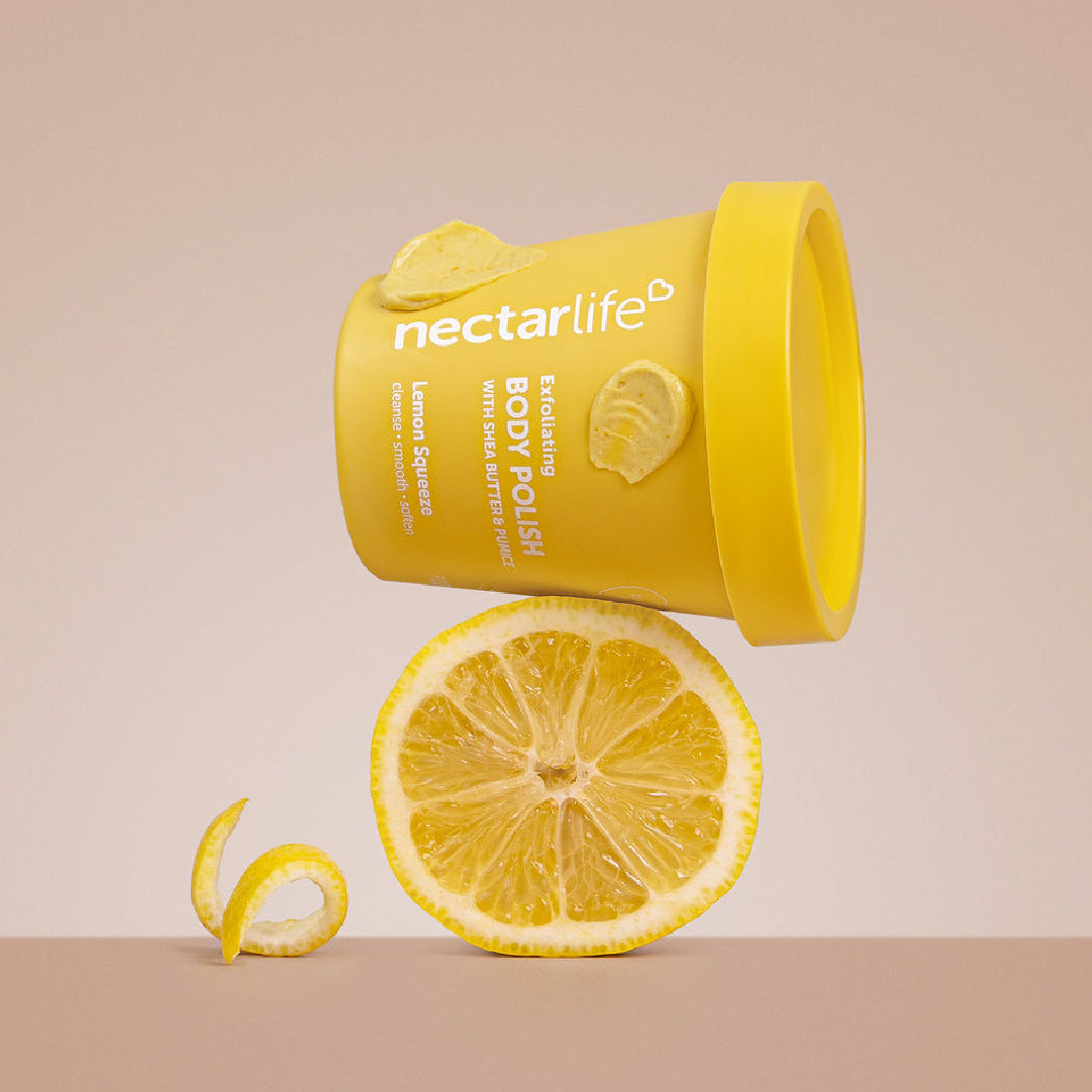 Nectar Life Body Polish Lemon Squeeze scent, yellow tub styled with fresh lemons on warm tan background, exfoliating body polish with shea butter and pumice