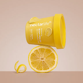 Nectar Life Body Polish Lemon Squeeze scent, yellow tub styled with fresh lemons on warm tan background, exfoliating body polish with shea butter and pumice