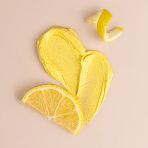 Nectar Life Body Polish texture close-up, yellow creamy pumice formula swiped on flat surface with lemon slices, ground pumice shea butter jojoba oil