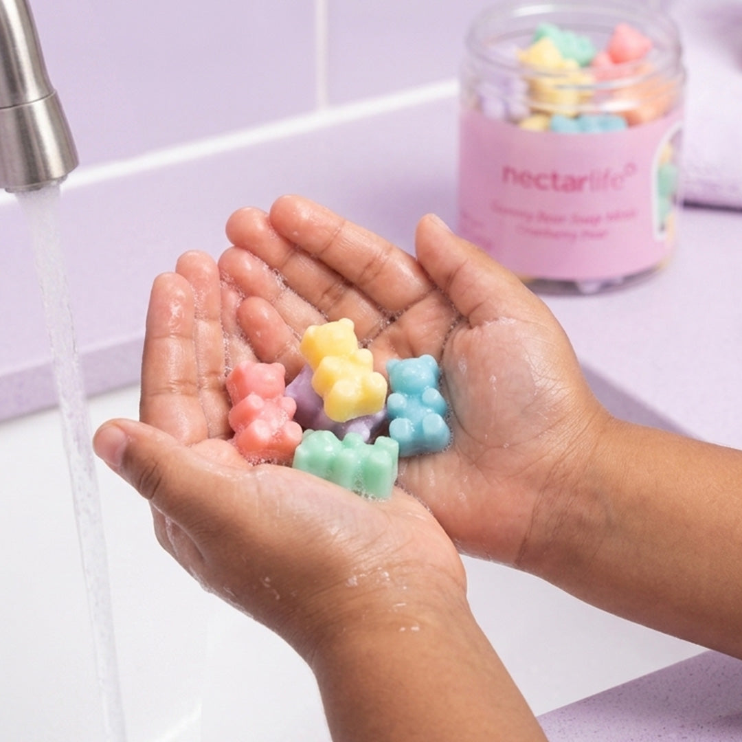 Hands lathering a Gummy Bear Soap Mini under running water by sink.