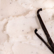 Close up texture shot of Nectar Life Vanilla Sugar Body Scrub showing white sugar granules with vanilla bean pods resting on top