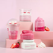 Nectar Life Strawberry Crème collection styled on pink pedestals, including the Moisturizing Bath Soak, Sugar Scrub with Coconut Oil, Nourishing Whipped Soap, Body Butter with Shea Butter, and Coconut Wax Candle, with fresh strawberries and whipped cream on a pink background