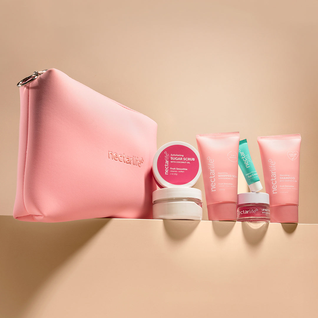 Nectar Life Glow on the Go Travel Kit contents laid flat, Fruit Smoothie scent, pink zip pouch, travel-size whipped soap with sweet almond oil, body scrub, shea body butter with avocado oil, shampoo, lip butter, eye cream, handmade in USA