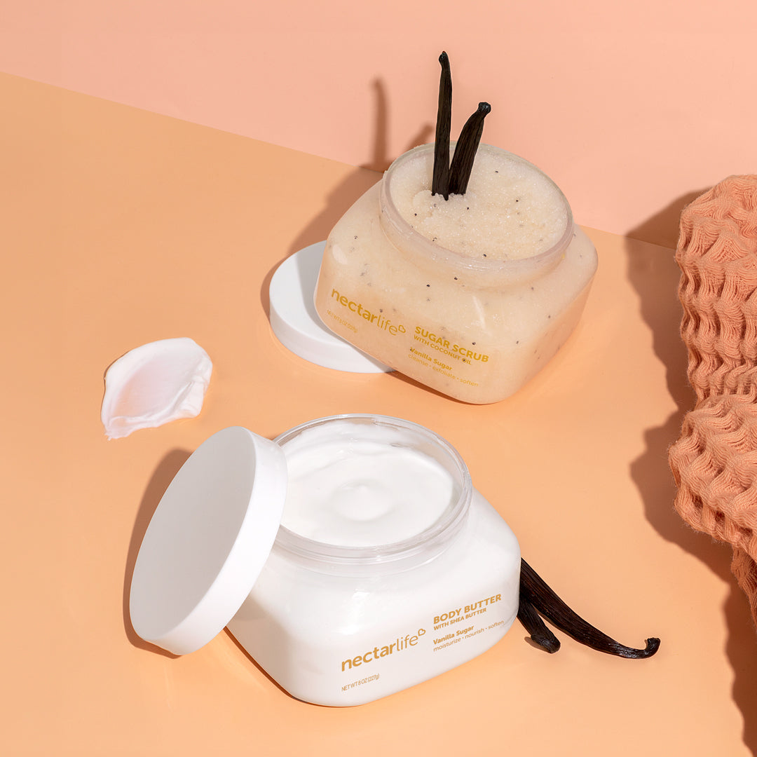 Product shot of Vanilla Sugar Scrub & Butter Duo by Nectar Life, open jars of Sugar Scrub with Coconut Oil and Body Butter with Shea Butter, 8oz each, styled with vanilla bean pods and a body butter swatch on a peach background