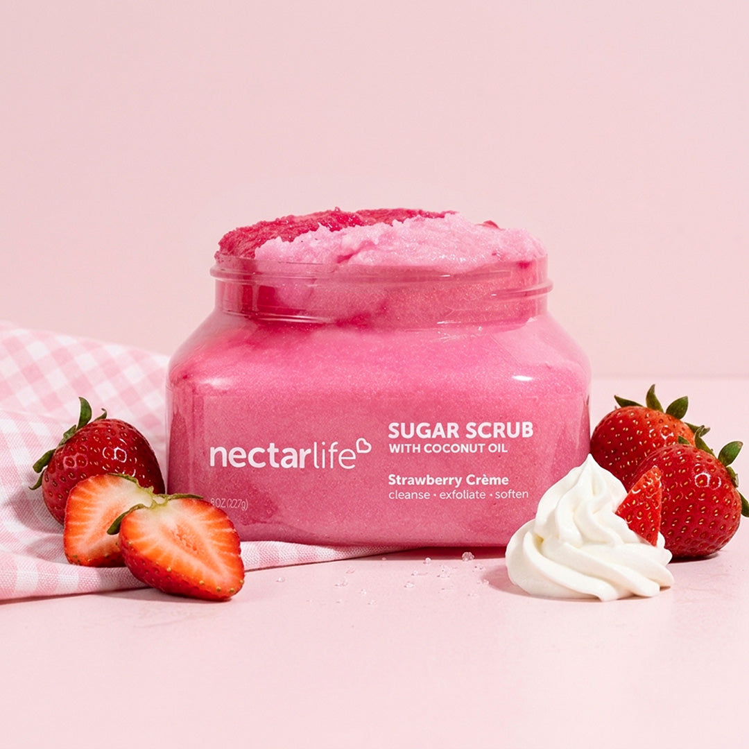 Strawberry Crème Sugar Body Scrub jar by Nectar Life styled with fresh strawberries and whipped cream on a pink gingham background, 8oz
