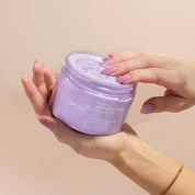 Hands cradling an open jar of Nectar Life Lavender Blossom Nourishing Whipped Soap and Shave Butter 10oz with pink manicured fingers dipping into the lavender whipped soap on a warm beige background