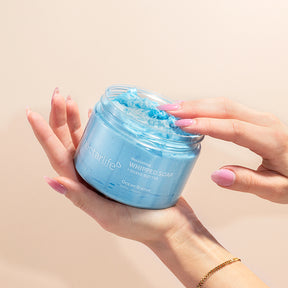 Hands cradling an open jar of Nectar Life Ocean Breeze Nourishing Whipped Soap and Shave Butter 10oz with pink manicured fingers dipping into the blue whipped soap on a warm beige background