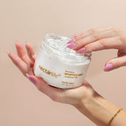 Hands cradling an open jar of Nectar Life Vanilla Sugar Nourishing Whipped Soap and Shave Butter 10oz with pink manicured fingers dipping into the white whipped soap on a warm beige background