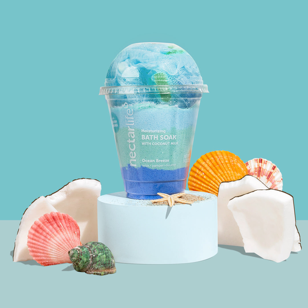 Ocean Breeze Moisturizing Milkshake Bath Soak by Nectar Life, layered blue powder soak with coconut milk in a dome-lid cup with loofah topper, styled with seashells, coconut pieces, and a starfish on a blue background, 9oz