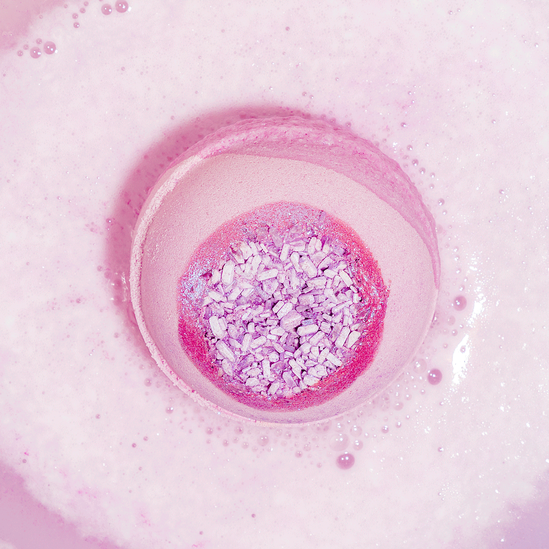 Nectar Life Surprise Ring Bath Bomb fizzing in pink water overhead view, hidden ring revealed as bomb dissolves, Epsom salt and coconut oil