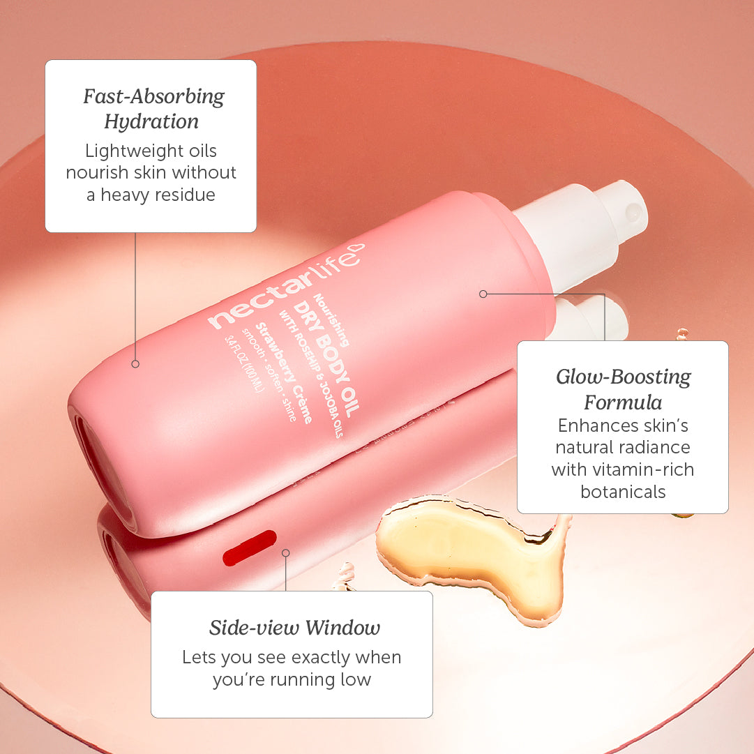Strawberry Crème Dry Body Oil spray bottle next to fresh strawberries, showing lightweight oil texture with rosehip and jojoba, 3.4 fl oz