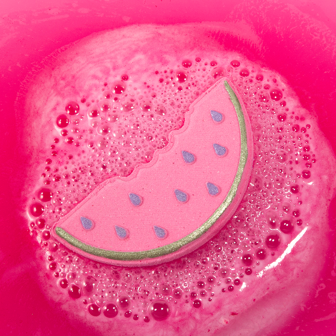 Nectar Life Fresh Watermelon Slice Bath Bomb floating in pink fizzing bath water, watermelon-shaped bath bomb with silver rind and purple seed details dissolving in a bubbly soak