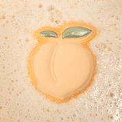 Nectar Life Juicy Peach Bath Bomb floating in warm fizzing bath water, peach-shaped bath bomb with glittery green leaf detail dissolving in a bubbly soak