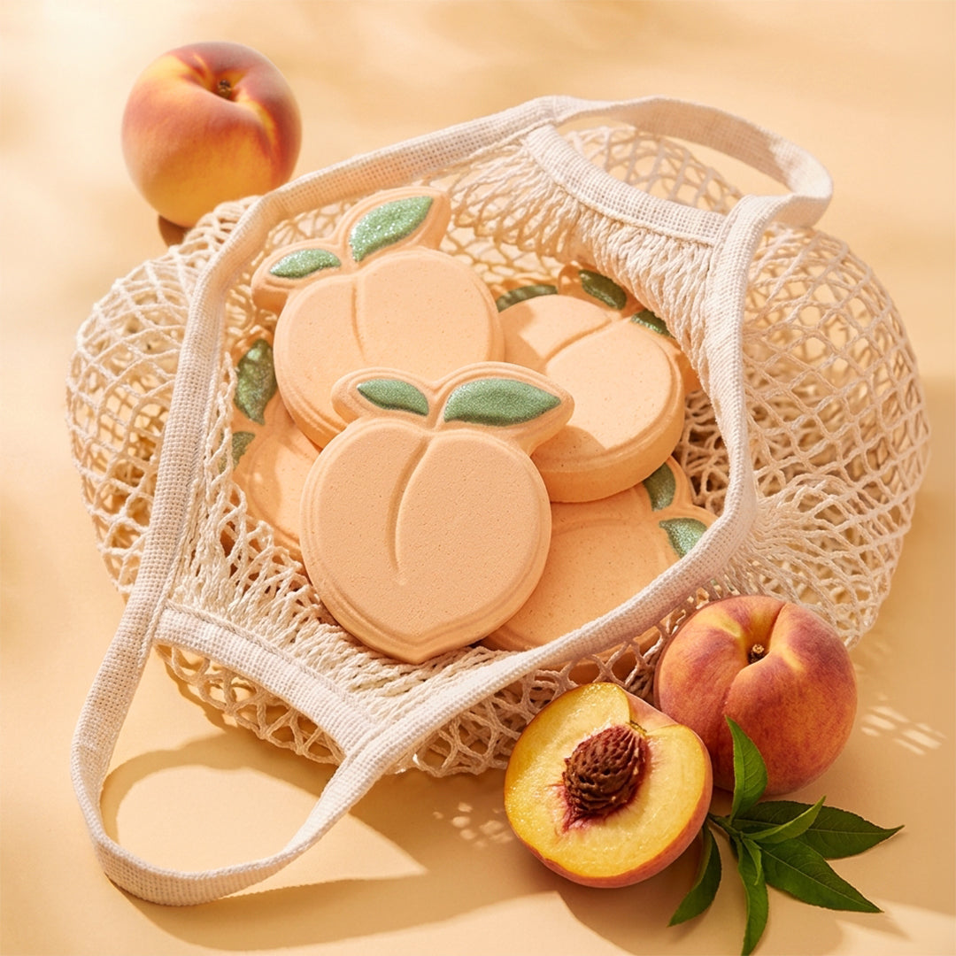 Nectar Life Juicy Peach Bath Bombs in a cream mesh tote bag surrounded by fresh peaches on a warm golden background