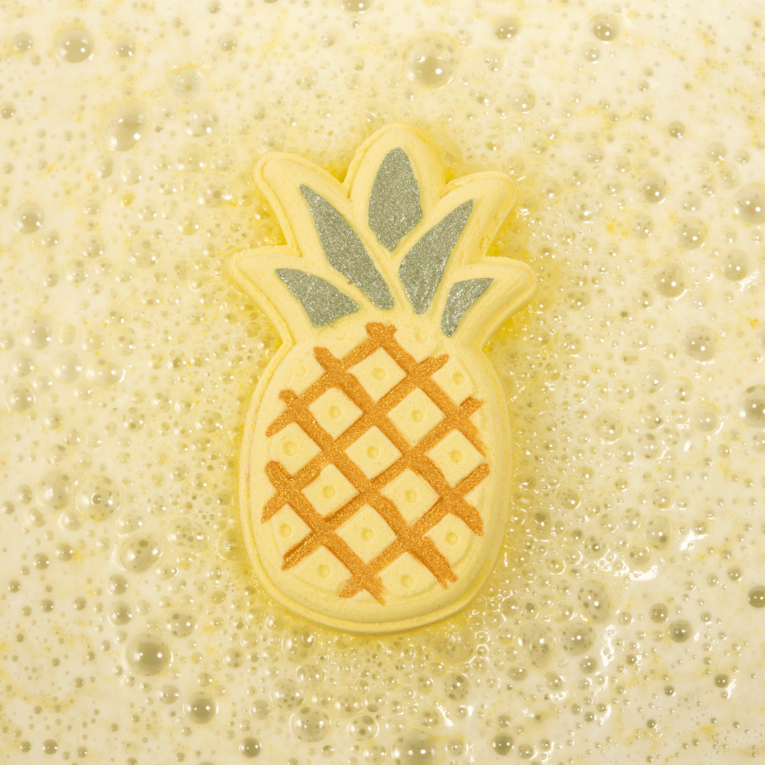 Nectar Life Tropical Pineapple Bath Bomb floating in golden fizzing bath water, pineapple-shaped bath bomb with glittery green crown dissolving in a bubbly soak