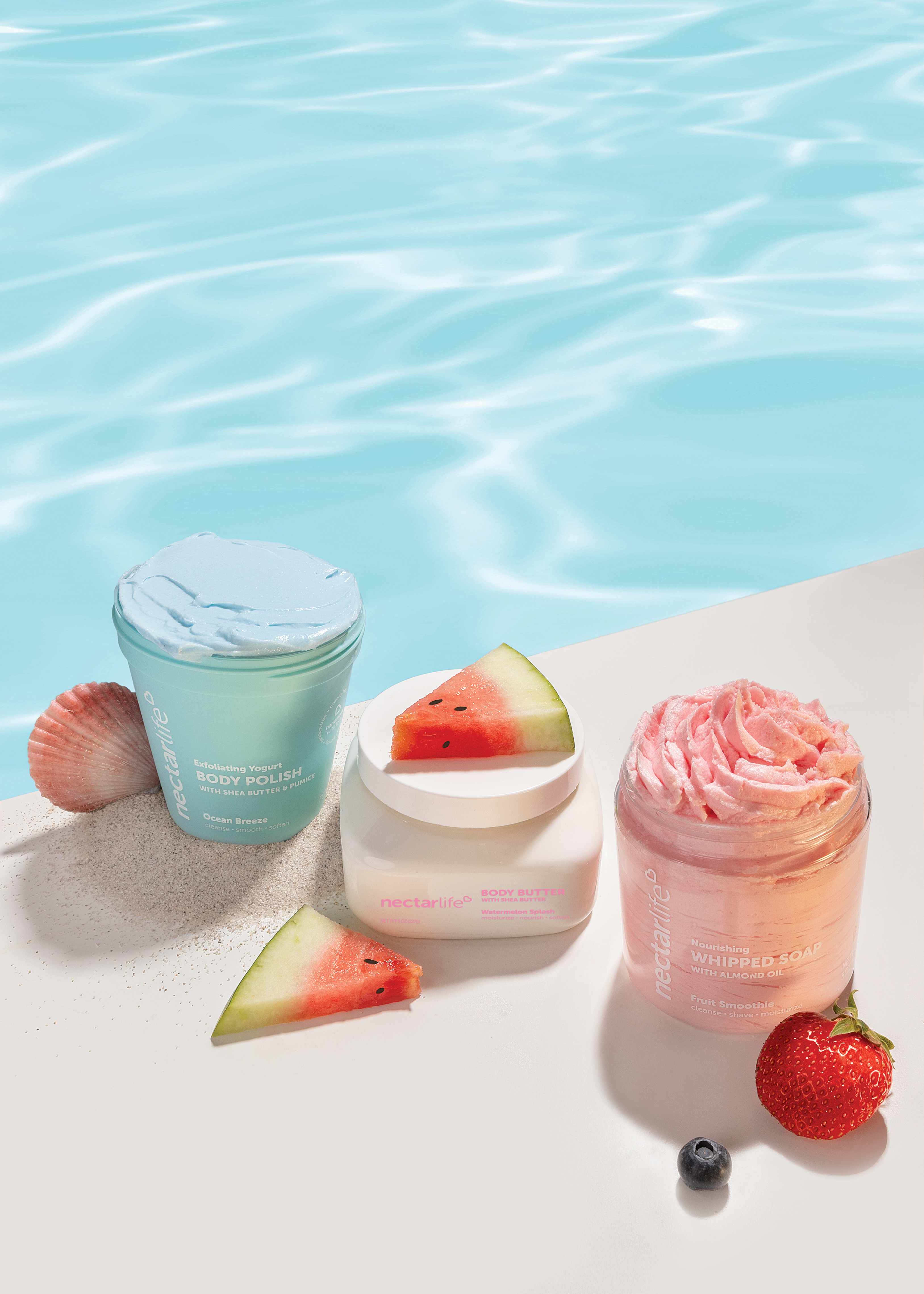 Nectar Life Ocean Breeze Body Polish, Watermelon Splash Body Butter, and Fruit Smoothie Whipped Soap arranged poolside with watermelon slices, a seashell, and fresh berries