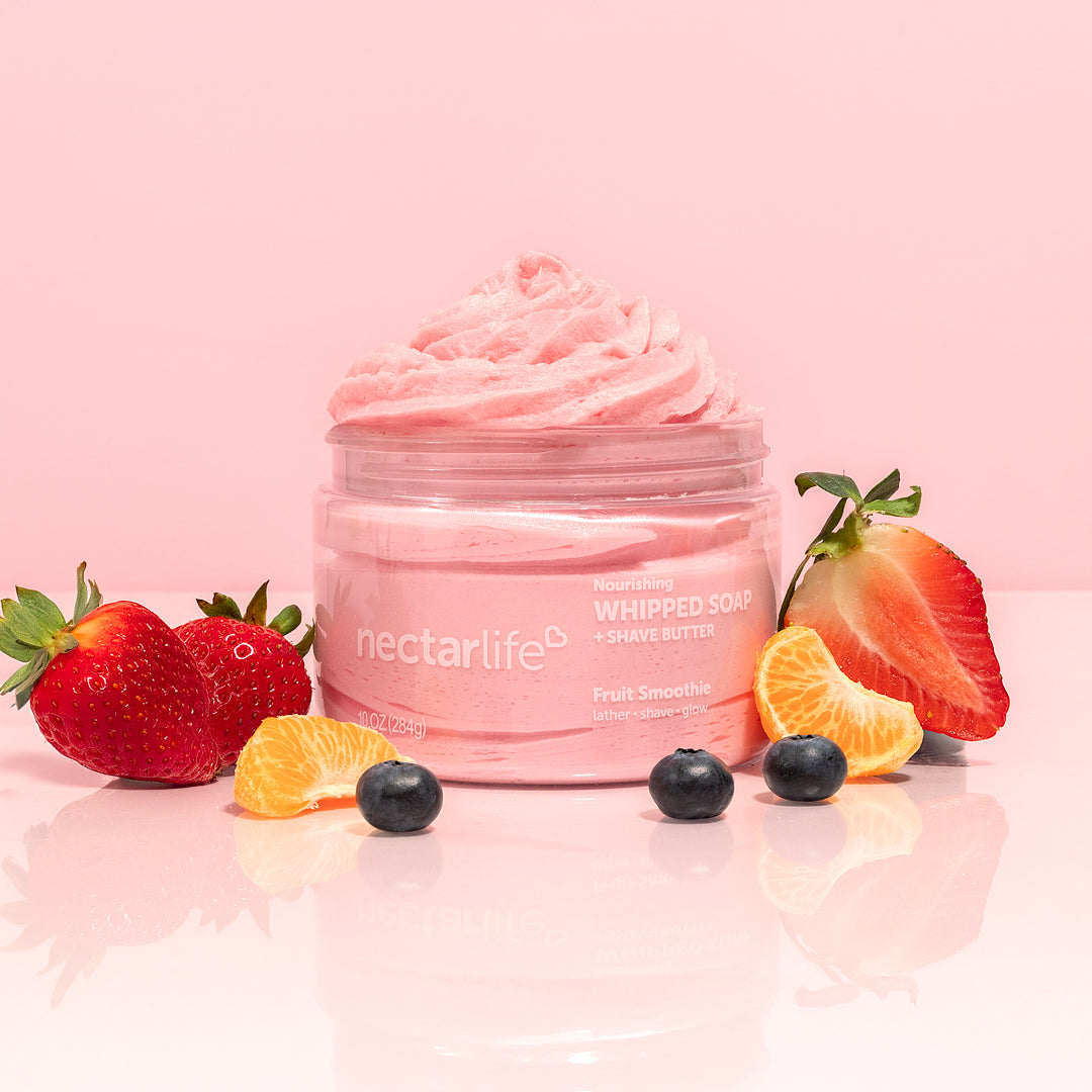 Nectar Life Fruit Smoothie Nourishing Whipped Soap and Shave Butter 10oz jar with whipped pink soap piled high, surrounded by fresh strawberries, blueberry, and mandarin orange segments on a soft pink background
